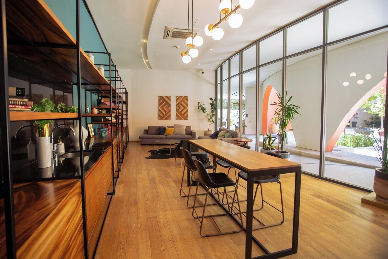 Um interior moderno com uma longa mesa de madeira, cadeiras pretas, um sofá e uma estante.