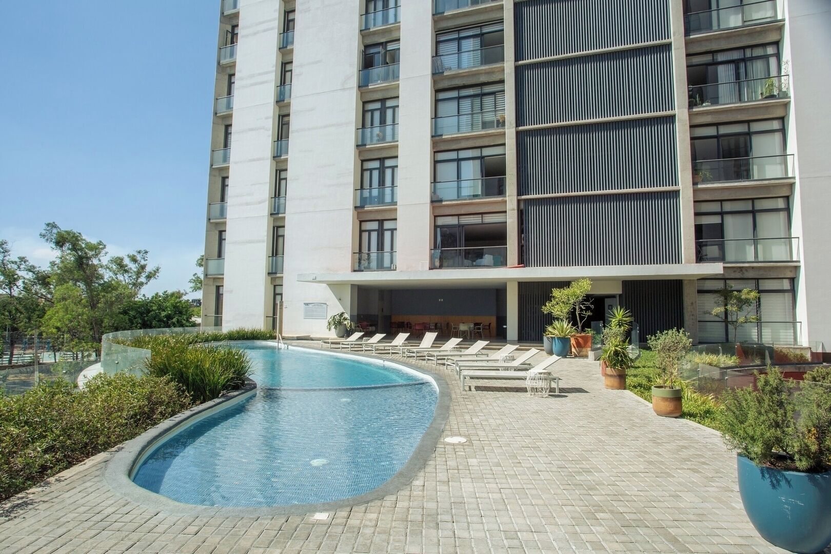 A modern hotel with a swimming pool, lounge chairs, and potted plants.