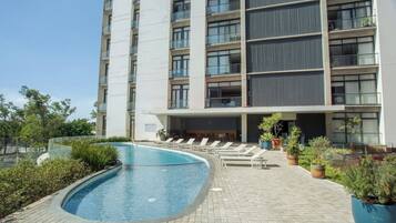 A modern hotel with a swimming pool, lounge chairs, and potted plants.