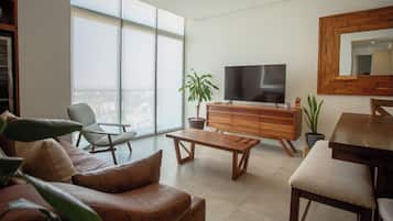 Uma sala de estar moderna com um sofá, um banco, uma TV e um espaço de refeições.