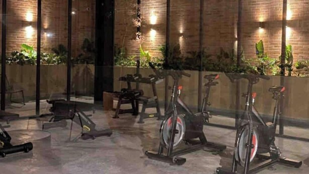 Een sportschool met hometrainers en fitnessapparatuur, bakstenen muren en binnenshuis planten.