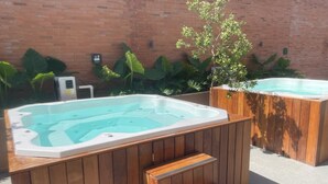 Twee bubbelbaden met houten trap, een bakstenen muur en grote groene planten op de achtergrond.