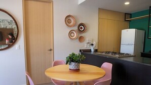 Een eethoek met een ronde tafel, vier stoelen, een kamerplant en een keuken op de achtergrond.