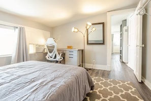 A bedroom with a bed, a desk, a chair, a standing lamp, and a mirror. - Simple Comfort - Metro Station - Work Desk (Pasadena)