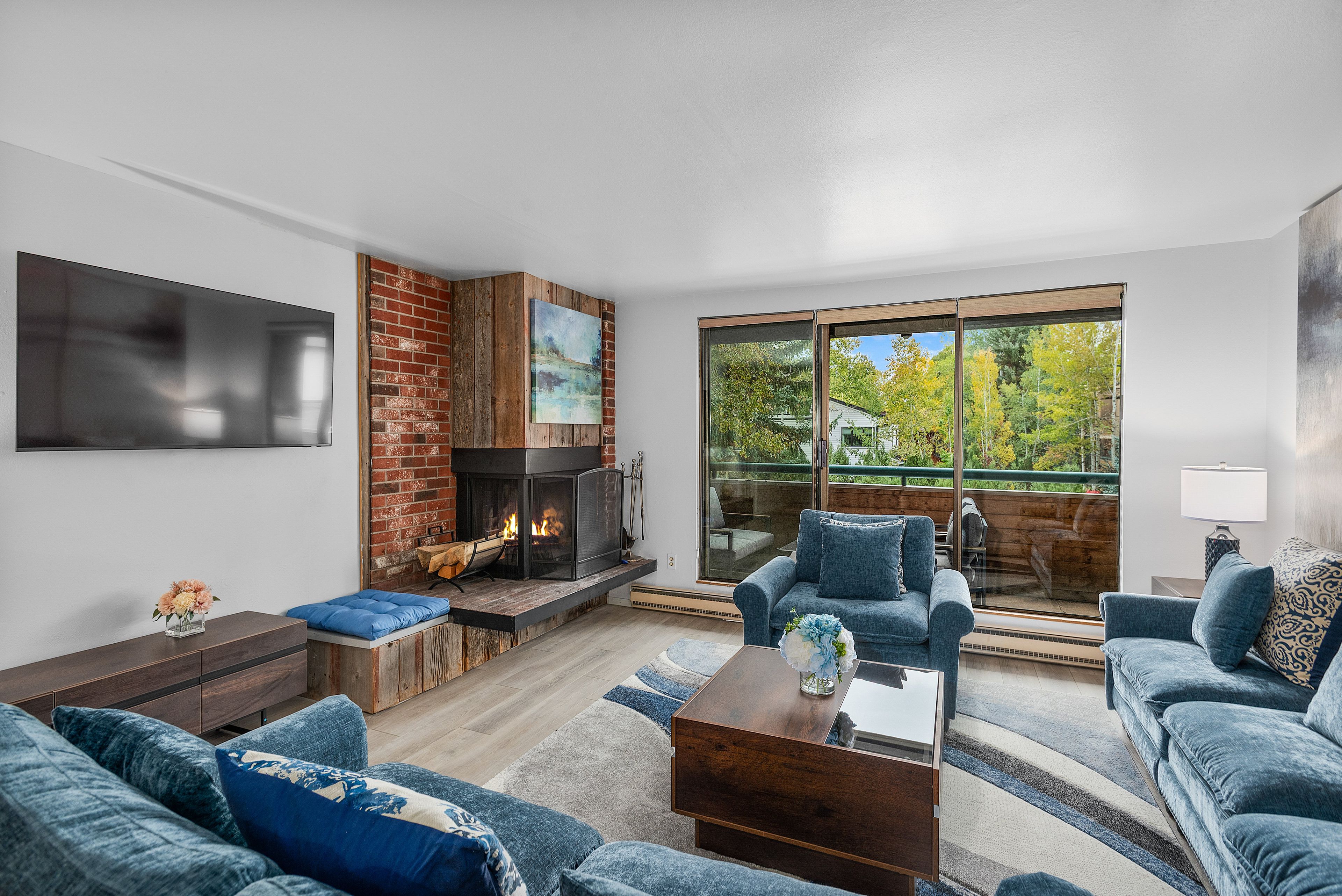 Living room at 1028 E. Hopkins in Aspen with a brick and reclaimed wood fireplace, blue sectional, and balcony doors