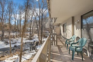 Ein Balkon mit Blick auf eine verschneite Landschaft und einen Fluss, mit zwei grünen Plastikstühlen und einem Holztisch.