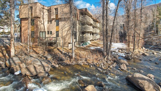 Un edificio con varios balcones que dan a un río, rodeado de árboles y rocas.