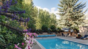 Una piscina rodeada de exuberante vegetación y árboles, con mobiliario de exterior y un cielo despejado.