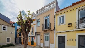 Une cour pavée avec un arbre, un banc et des bâtiments colorés dotés de balcons.