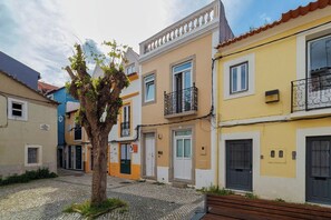 Ein Kopfsteinpflasterhof mit Baum, Bank und farbenfrohen Gebäuden mit Balkonen.
