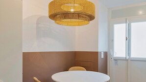 Une pièce avec une table ronde blanche, une chaise jaune, un luminaire en fibres tressées et une porte avec une fenêtre.