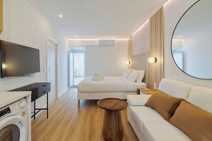 Ein modernes Hotelzimmer mit Fernseher, Bett, Sofa, rundem Spiegel und Waschmaschine.