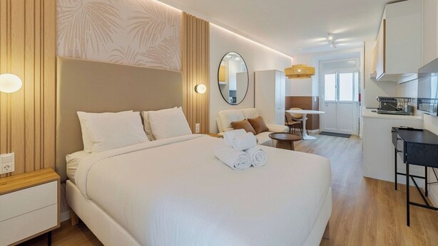 Une chambre d’hôtel avec un grand lit, un bureau, une chaise, un miroir rond et une kitchenette.