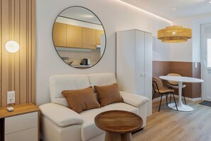 Ein modernes Wohnzimmer mit einer Couch, einem runden Couchtisch, einem Essbereich mit Tisch und Stühlen, einer im Spiegel sichtbaren Küche und einer Chandelier.