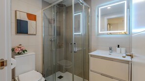 A modern bathroom with a glass-enclosed shower, a toilet, a sink with a mirror, and a framed abstract painting on the wall. - Bright and Fantastic Studio - Suitable for Ambassadors (Madrid)