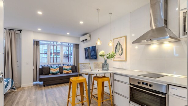 A modern kitchen with a built-in oven, a dining area with stools, a sofa, and a large window. - Bright and Fantastic Studio - Suitable for Ambassadors (Madrid)