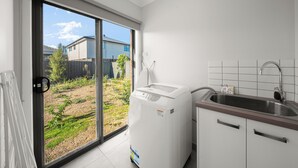 Una cocina con lavadora incorporada, un lavabo y un ventanal corredera que da a un patio trasero.