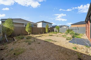 A residential backyard with a gravel area, a wooden fence, and a house with a brick exterior. - Werribee Nature Sounds：4B Family Getaway 2Garage (Werribee)