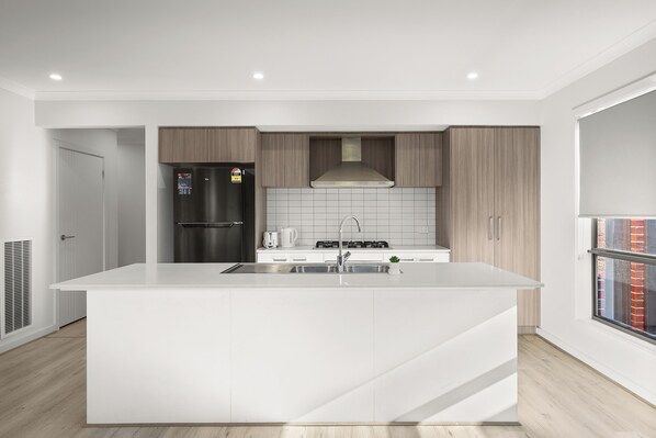 A modern kitchen with a central island, stainless steel appliances, and a view of the city through a window.