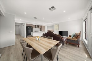A modern living room with a wooden dining table, leather chairs, a sofa, and a television.