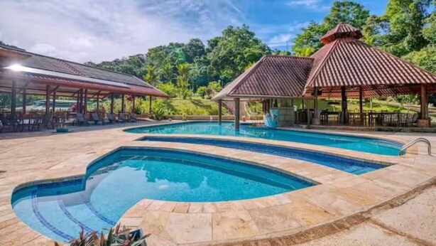 Piscina com design curvo, rodeada por azulejos de pedra.