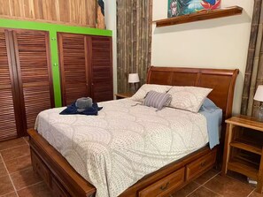 Ein Schlafzimmer mit einem hölzernen Bett, einem Nachttisch, einer Lampe, einem Kleiderschrank und einer Wand in Grüntönen.