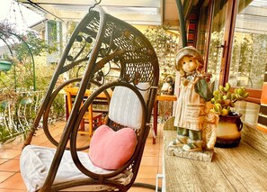 A wicker chair with a cushion, a small table, and a potted plant on a balcony. - 5 mins to largest park, 2 mins to highway & mall. Quality home, pet-friendly. (Glen Waverley)