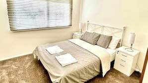 A bedroom with a bed, bedside tables, a lamp, and a window with blinds.