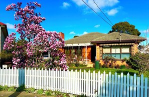 A residential house with a white picket fence, a porch, and a magnolia tree in bloom. - 5 mins to largest park, 2 mins to highway & mall. Quality home, pet-friendly. (Glen Waverley)
