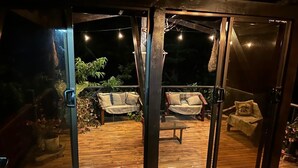Eine Holzterrasse mit zwei Sofas und einem Tisch, umgeben von Glastüren.