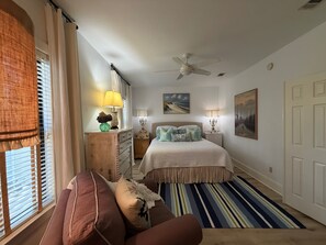 A bedroom with a bed, a ceiling fan, a window with blinds, a dresser, and a bedside table with lamps. - Sea Gypsy - 4BR, Walk to Beach and iconic eateries, Pet Friendly, Hot Tub, Bikes (Santa Rosa Beach)