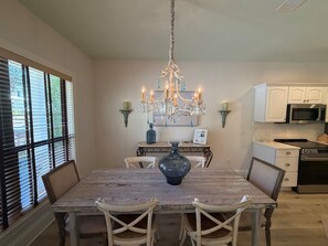 A dining area with a chandelier, a table, chairs, a vase, and a kitchen in the background. - Sea Gypsy - 4BR, Walk to Beach and iconic eateries, Pet Friendly, Hot Tub, Bikes (Santa Rosa Beach)