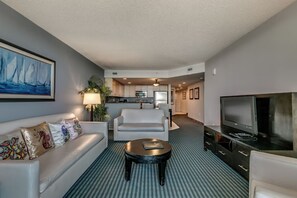 A hotel room with a living area, a sofa with decorative pillows, a coffee table, a TV, a kitchen area, and a hallway. - Stunning Oceanfront King Suite at Oceans One Resort 9th Floor (Myrtle Beach)