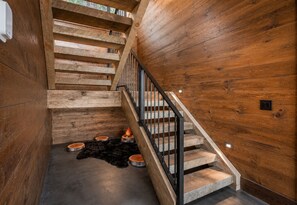Un escalier en bois avec une rampe en métal, un tapis noir à poils longs et des bols en bois posés sur le sol.