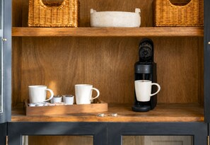 Une étagère en bois avec des paniers en osier, une machine à café et des tasses blanches.