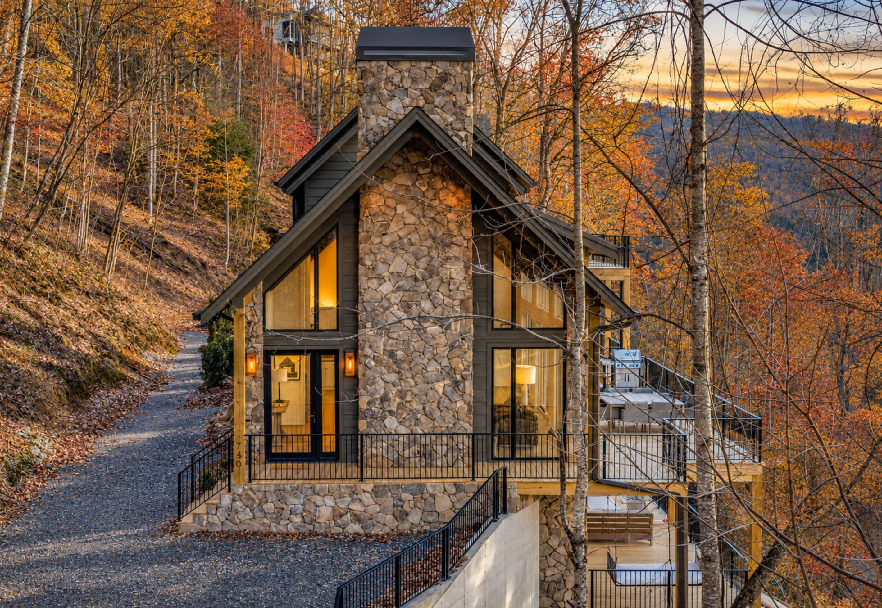 A stone house with a stone chimney, large windows, and a wooden deck.