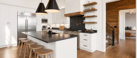 Une cuisine moderne dotée d’un grand îlot central, de tabourets de bar, d’un réfrigérateur en acier inoxydable et de poutres en bois au plafond.