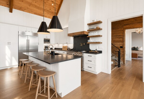 Une cuisine moderne dotée d’un grand îlot central, de tabourets de bar, d’un réfrigérateur en acier inoxydable et de poutres en bois au plafond.