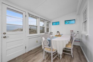 A room with a white door, a table with chairs, and two windows with artwork. - Beachfront Charm in Beautiful East Sandwich (East Sandwich)