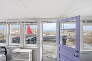 A room with large windows, a door, and a small table. - Beachfront Charm in Beautiful East Sandwich (East Sandwich)