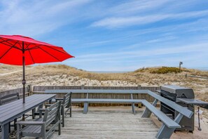 A wooden deck with benches and a barbecue grill, overlooking a beach with dunes. - Beachfront Charm in Beautiful East Sandwich (East Sandwich)