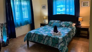 Une chambre à coucher avec un lit, deux tables de chevet, un ventilateur de plafond et des rideaux.