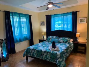Ein Schlafzimmer mit einem Bett, zwei Nachttischen, einem Deckenventilator und Vorhängen.