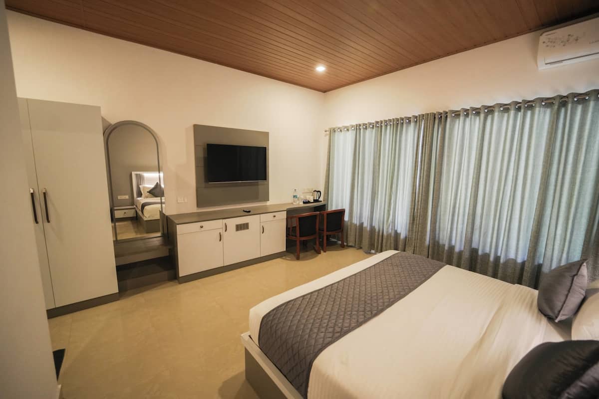 A hotel room with a bed, a desk with a chair, a television, and a wardrobe.