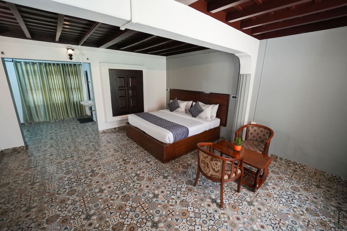 A bedroom with a bed, a chair, a small table, and a door leading to another room.