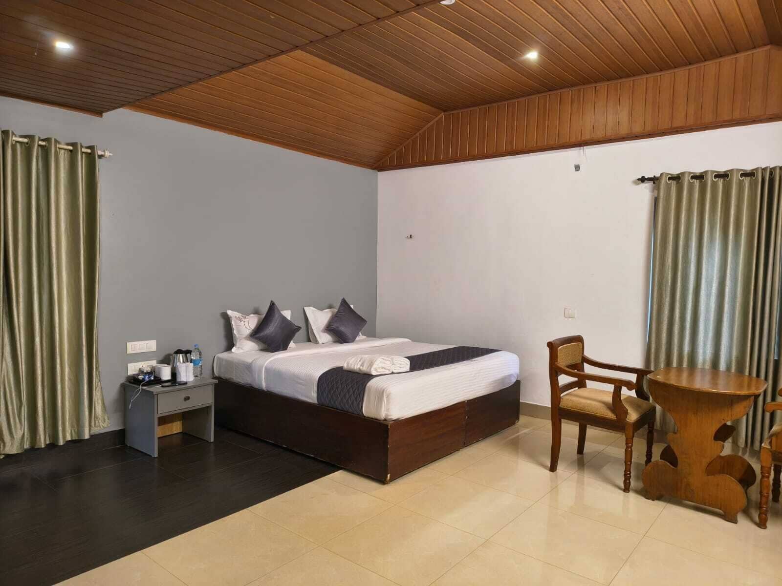 Een slaapkamer met een houten plafond, een bed met kussens, een nachtkastje, een stoel en een tafel.