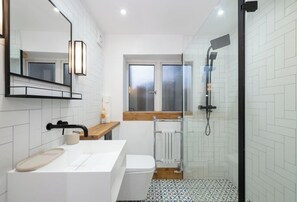 Un baño moderno con un lavamanos blanco, un espejo, una ducha y una ventana.