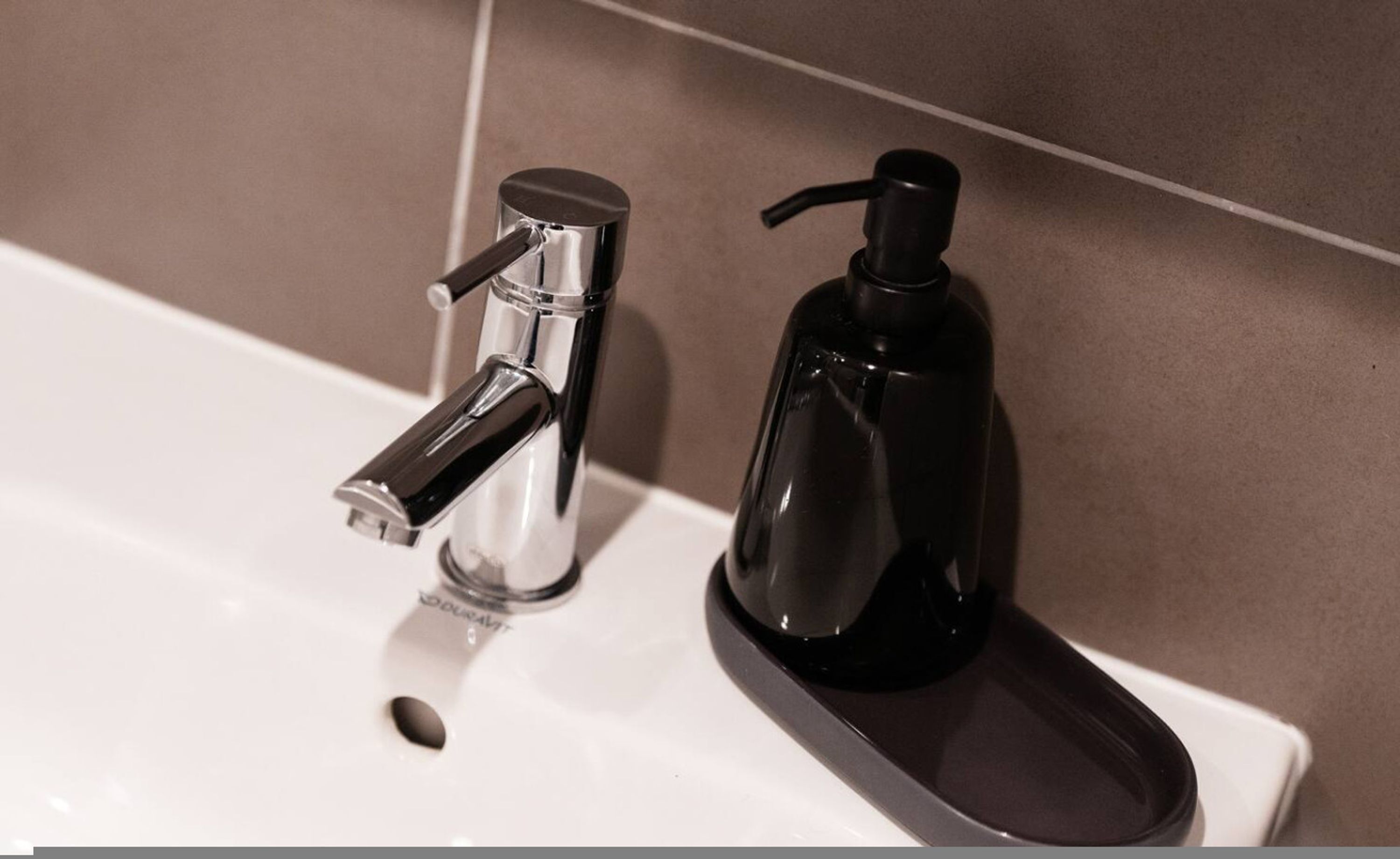 Un lavamanos de baño con un grifo moderno y un dispensador de jabón negro.