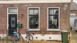 Un bâtiment en briques avec deux fenêtres, une porte et une poubelle verte.