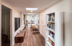 A narrow hallway with a wooden bench, a bookshelf, and a door leading to another room.